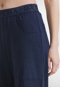 Granatowe spodnie o szerokich nogawkach z miękkim elastycznym paskiem, wyposażone w boczne kieszenie i subtelne detale szwów. Wykonane z lekkiego materiału.