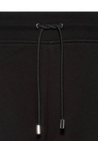 Zwarte joggingbroek met een geribde tailleband, voorzien van een zwarte trekkoord met zilveren metalen punten. De stof heeft een gladde textuur.