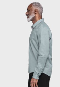 Hellblaues Langarmhemd mit Button-Down-Kragen, ausgestattet mit einer Brusttasche und subtil strukturiertem Stoff.