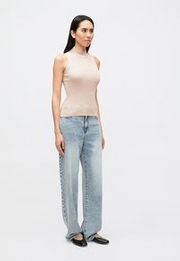 Gaiši bēša ribota bezroku topiņa, kas apvienota ar gaismā ziliem platām džinsu biksēm. Melni, smaili dzīvokļi noslēdz tērpu. Vienkāršs dizains, minimālas detaļas.