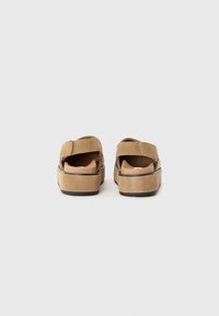 Tan suède sandalen met een brede band, gevoerde binnenzool en een chunky platformzool. Kenmerken zijn een open achterkant en textuuraccenten aan de zijkanten.