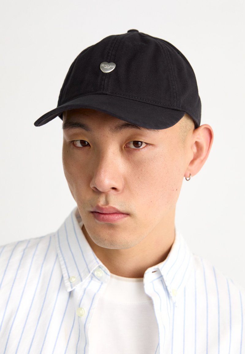 Black baseball cap made of cotton, featuring a small silver logo on the front. The cap has a curved brim and an adjustable strap at the back.