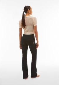 Top de punto corto en color beige claro combinado con pantalones acampanados negros que cuentan con bolsillos traseros y un pequeño acento de logo.