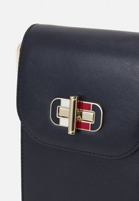 Námořnická kožená kabelka se zlatým zapínáním, která obsahuje červené, bílé a námořnické akcenty. Hladký povrch s zakřivenými okraji a prošívanými detaily.