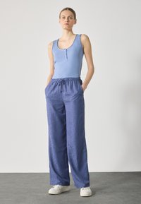 Lyseblå ribbestrikket tanktop med tre knapper, kombinert med vidt benede mørkeblå mønstrede bukser og hvite joggesko. Minimalistisk design.