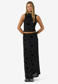 Svart tvådelad outfit med en ärmlös kort topp och en lång kjol, båda prydda med ett blommönster och genomskinlig textur.