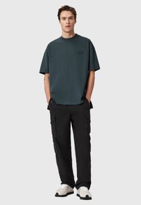 Ciemnozielona, oversize t-shirt z okrągłym dekoltem i krótkimi rękawami, w połączeniu z czarnymi spodniami cargo z wieloma kieszeniami i luźnym krojem.