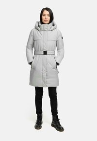 Lysegrå lang frakke med indsnøret talje, hætte, store lommer og bælte. Kombinationen med sorte bukser og snørebåndsstøvler.