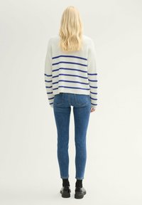 Suéter de punto blanco con rayas horizontales azules, combinado con jeans ajustados azules y zapatos de plataforma negros. Vista desde la parte posterior.