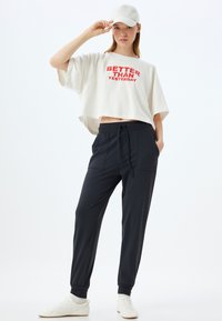 Witte cropped t-shirt met rode tekst, gecombineerd met zwarte joggers met twee voorzakken en elastische boorden. Witte sneakers maken de look compleet.