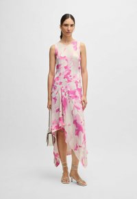 Asymmetrisches Kleid aus leichtem Stoff, mit einem floralen Muster in Pink und Weiß, fließendem Fall und knielangem Saum.