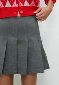 Grijze geplooide rok van textuurstof, met een elastische tailleband en een uitlopende vorm, gecombineerd met een trui in rood en roze met een patroon.