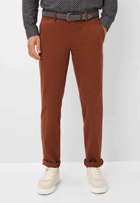 Braune Baumwollhose mitSlim Fit, umgeschlagenem Saum und Fronttaschen, kombiniert mit einem strukturierten dunkelblauen Hemd und hellen Sneakers.
