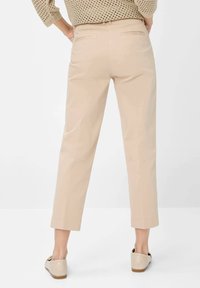 Beiga byxor i ankellängd med en slät textur, sidofickor och sydda detaljer vid fållen, matchat med ljusa slip-on skor.