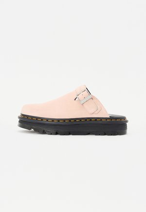 Light pink suede slip-on shoe with black thick sole, yellow stitching, and silver buckle on the upper side.