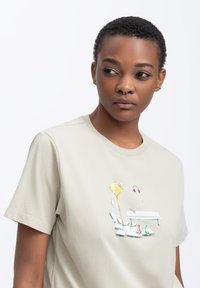 Lichtbeige T-shirt van katoen met korte mouwen en een ronde hals. Bevat een kleurrijke geborduurde grafiek op de borst.