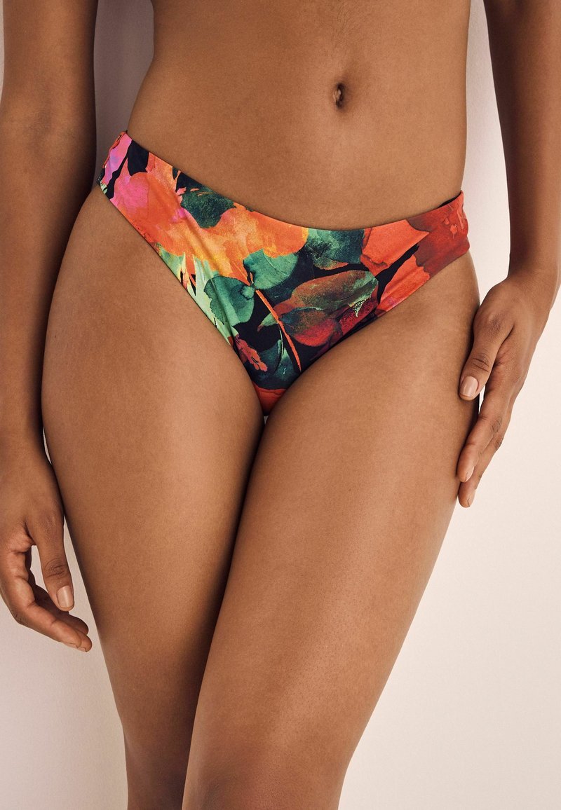 Gėlių bikini apatinė dalis, su ryškiomis raudonos, oranžinės ir žalios spalvų atspalviais, glotnia tekstūra ir aukštu įpjovimu, užtikrinančiu minimalų dengimą.