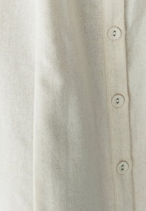 Lichtbeige knoopsluiting shirt van textuurstof, met vier gelijkmatig verdeelde knopen langs de voorkant.