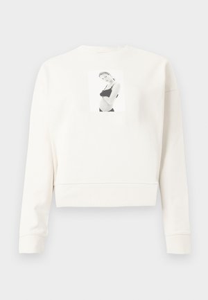 Sweatshirt court à manches longues blanc avec une photo imprimée en noir et blanc d'une femme en sous-vêtements noirs au centre avant.