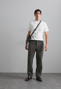 White short-sleeve t-shirt, dark grey wide-leg trousers, and black crossbody bag. Model wears brown shoes, standing against a neutral backdrop.