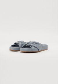 Des sandales à glissière bleu clair avec un design noué sur le dessus, une texture lisse et une semelle plate avec un bord de couleur naturelle.