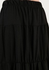 Black tiered skirt made of textured fabric, featuring an elastic waistband. The surface shows a subtle crinkled pattern and soft draping.
