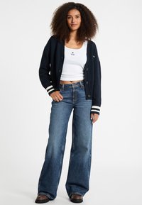 Cardigan a maglia blu navy con polsini bianchi a righe, bottoni e vestibilità rilassata, abbinato a jeans blu a gamba larga a vita alta e una canotta bianca.
