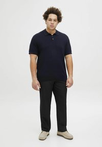 Jūrinės tamsiai mėlynos spalvos trumpomis rankovėmis polo marškiniai su tekstūruotu mezgimo raštu, derinami su juodomis kelnių ir šviesiai rudos spalvos šlepetėmis. Paprastas ir tvarkingas įvaizdis.