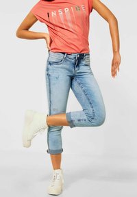 Korálové tričko s potiskem "INSPIRE", modré džíny s ohrnutými lemy a bílé vysoké tenisky. Ležérní střih s mírným umytím a čistými liniemi.