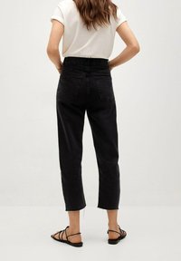 Czarne dżinsy z wysokim stanem, o prostym kroju, skrojone na długość do kostek, z postrzępionym dołem. Dwie tylne kieszenie, w połączeniu z płaskimi sandałami na paski.