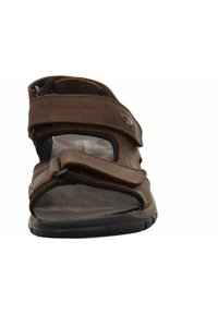 Brown leather sandal with wide adjustable straps, textured fabric lining, rubber sole, and sliding buckle detail. Open-toe design.