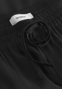 Schwarze Shorts mit elastischem Bund, Zugband und einem weißen Etikett mit "GABBA"-Text. Glatte Stoffoberfläche.