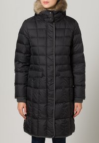 Zwarte, gewatteerde pufferjas met een nepbontkraag, voorzakken en ribgebreide manchetten. Knie-lange uitvoering met een verborgen ritssluiting.