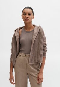 Bruine gebreide hoodie met geribbelde textuur en opgerolde randen, gecombineerd met een aansluitend bruin tanktopje en beige broek.