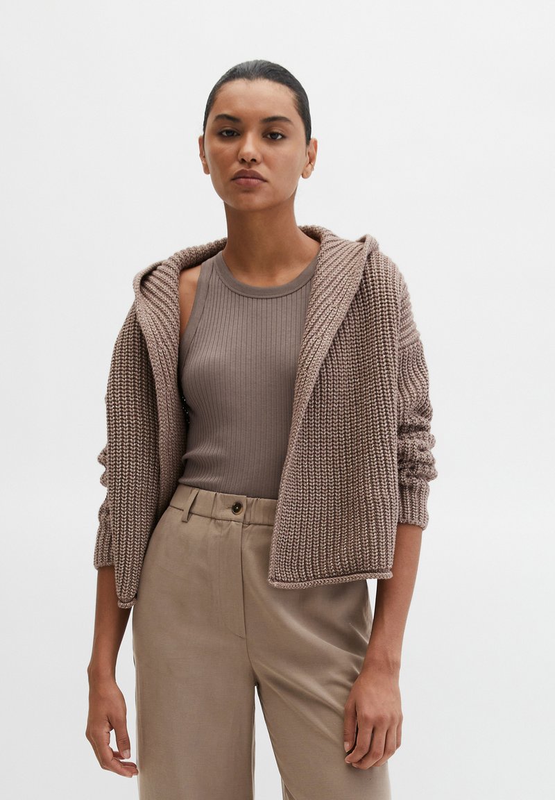 Bruine gebreide hoodie met geribbelde textuur en opgerolde randen, gecombineerd met een aansluitend bruin tanktopje en beige broek.