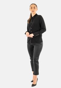 Camicia nera a maniche lunghe con colletto e chiusure a bottone color oro, abbinata a pantaloni neri aderenti e décolleté nere con punta.