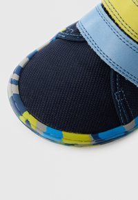 Spordisandaal tumesinise kangast pealsega, helesinise rihma ja värvika mustrilise tallaga kollases, sinises ja hallis. Tekstuuriga viimistlus, kindel istuvus.