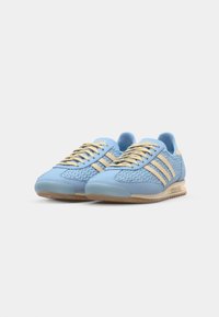 Zapatillas deportivas de color azul claro con detalles tejidos, tres franjas beige, cordones redondos y suela de goma texturizada.
