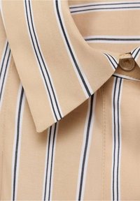 Col de chemise beige à rayures verticales noires et blanches, montrant un bouton et la texture du tissu en gros plan.