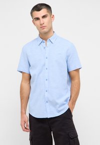 Camisa de botón de manga corta azul claro con una textura suave y un cuello clásico; presenta un logo sutil y un dobladillo redondeado.