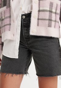 Cardigan peludo de cuadros rosa y gris sobre una camiseta blanca, combinado con shorts de mezclilla negros de talle alto con dobladillos deshilachados y un botón clásico.