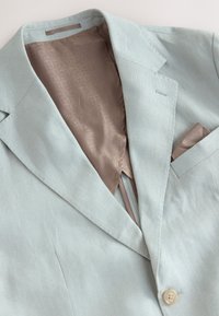 Blazer azzurro chiaro in tessuto strutturato. Caratteristiche notevoli includono una fodera beige setosa e un fazzoletto da taschino infilato nella tasca sul petto.