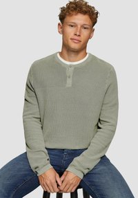 Lichtgroene longsleeve henley shirt met een textuurstof, voorzien van een ronde hals en een twee-knoopsluiting, gedragen met een blauwe spijkerbroek.