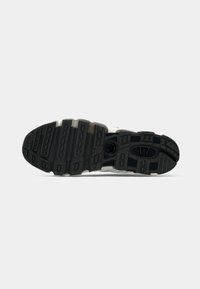 Black and gray rubber sole of a sneaker with patterned treads and circular cutout on a plain white background.