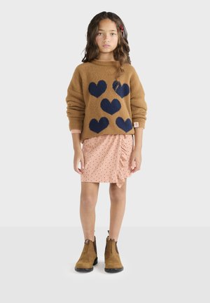 Suéter marrón con patrones de corazones marinos, falda de lunares rosas con fruncidos y botas de tobillo marrones con lados elásticos.