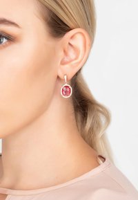 Orecchini con gemme rosse dal design sfaccettato, montati in metallo dorato, circondati da piccole pietre trasparenti, appesi a un perno curvo.