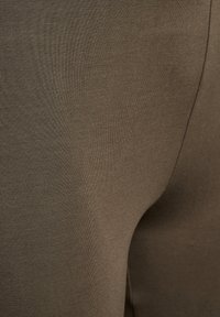 Olivgrüner, körpernaher Stoff, glatte Textur, gerippte Oberfläche, mit minimalen Nähten und einem enganliegenden Design, das für Sportbekleidung oder legere Nutzung geeignet ist.
