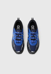 Des chaussures de sport bleu et noir avec un upper en maille, des accents blancs et des lacets à motifs, présentant un bout arrondi et une semelle en caoutchouc texturée.