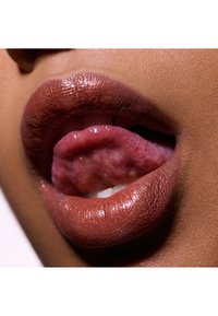 Kiiltelevät ruskeat huulet, joissa on rakenne, hieman raollaan, paljastaen vaaleanpunaisen kielen ja aavistuksen valkoisia hampaita lähikuvassa.