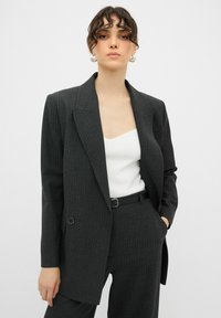 Blazer grigio scuro a righe sottili con rever a punta, dettaglio a un bottone e vestibilità oversize, abbinato a un top bianco con scollatura a barca.